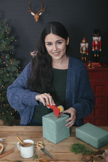 Porträt einer lächelnden jungen Frau, die ein Weihnachtsgeschenk einpackt - RTBF00507