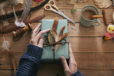 Woman decorating Christmas present with leaf and feathers, close-up - RTBF00510