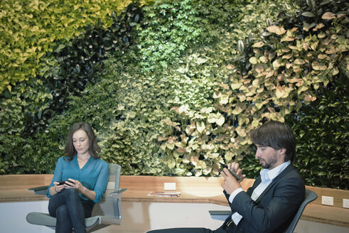 Geschäftsleute benutzen Smartphones vor einer grünen Pflanzenwand - WESTF21885