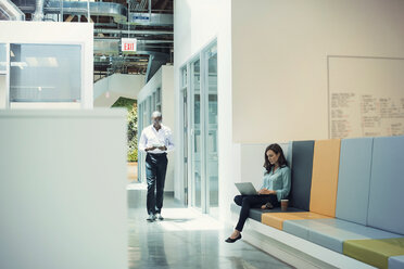 Woman working in lobby, colleague walking down corridor - WESTF21887