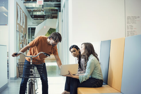 Junger Mann auf dem Fahrrad im Gespräch mit Kollegen am Laptop - WESTF21890