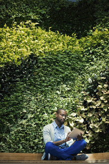 Junger Geschäftsmann mit digitalem Tablet vor einer grünen Pflanzenwand - WESTF21893