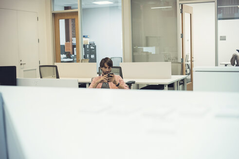 Mann arbeitet im Büro und schaut auf sein Smartphone - WESTF21919
