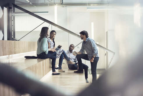 Junge Geschäftsleute, die auf einer Treppe sitzend diskutieren - WESTF21948
