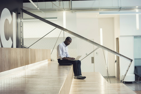 Geschäftsmann sitzt auf einer Treppe und benutzt einen Laptop, lizenzfreies Stockfoto