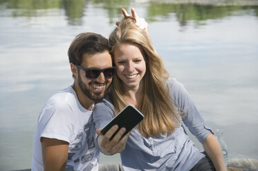 Verspieltes junges Paar an einem See, das ein Selfie macht - CRF02762