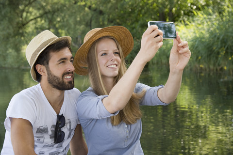 Lächelndes junges Paar an einem See, das ein Selfie macht, lizenzfreies Stockfoto