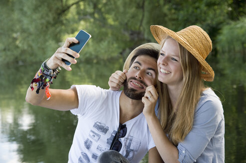 Verspieltes junges Paar an einem See, das ein Selfie macht - CRF02764