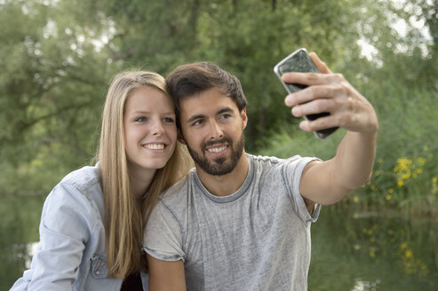 Lächelndes junges Paar an einem See, das ein Selfie macht - CRF02772