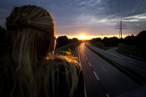 Woman looking at sunset behind motorway - BMAF00285