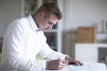 Junger Mann arbeitet an einem Bauplan am Schreibtisch - SGF02063