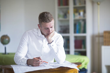 Junger Mann betrachtet einen Bauplan am Schreibtisch - SGF02064