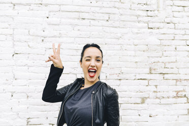 Portrait of young woman in front of brick wall making victory sign - GEMF01189