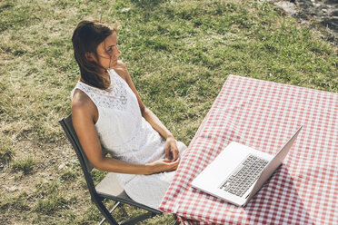 Young woman sitting at table on meadow with laptop - SBOF00261