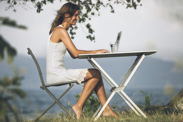 Italy, Lake Garda, young woman sitting at table with laptop - SBOF00264