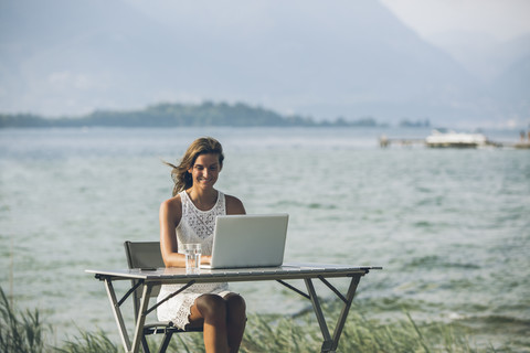 Italien, Gardasee, junge Frau sitzt am Tisch mit Laptop, lizenzfreies Stockfoto