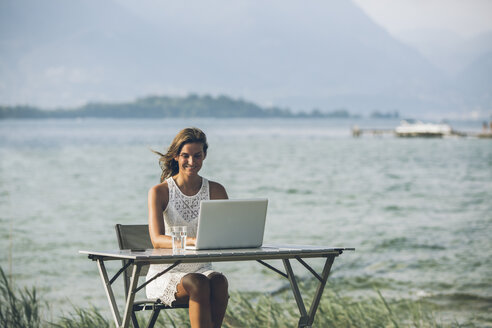 Italien, Gardasee, junge Frau sitzt am Tisch mit Laptop - SBOF00265