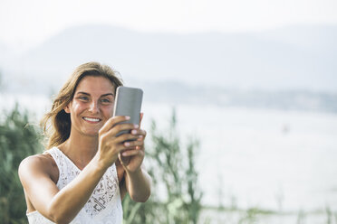 Italy, Lake Garda, young woman taking a selfie - SBOF00272