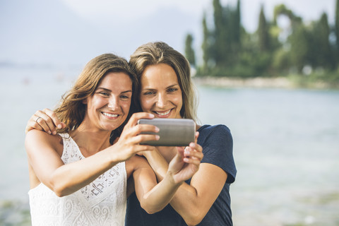 Italien, Gardasee, zwei junge Frauen machen ein Selfie, lizenzfreies Stockfoto