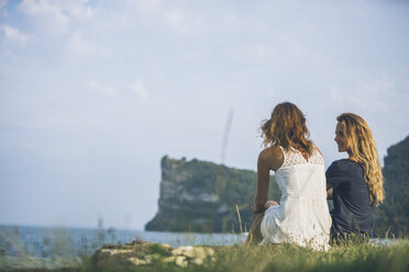 Italy, Lake Garda, two young women sitting at lakeshore - SBOF00280