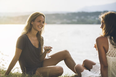 Italien, Gardasee, zwei junge Frauen sitzen am Seeufer mit einem Glas Wein - SBOF00281