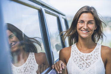 Porträt einer lächelnden jungen Frau, die sich an einen Campingbus lehnt - SBOF00292