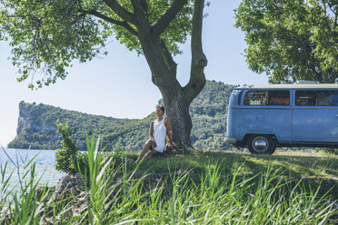 Italy, Lake Garda, woman sitting at camping bus at lakeshore - SBOF00295