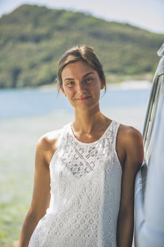 Italien, Gardasee, Porträt einer lächelnden jungen Frau, die sich an einen Campingbus lehnt, lizenzfreies Stockfoto