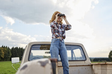 Frau steht auf einem Pick-up-Truck und schaut durch ein Fernglas - FMKF03175