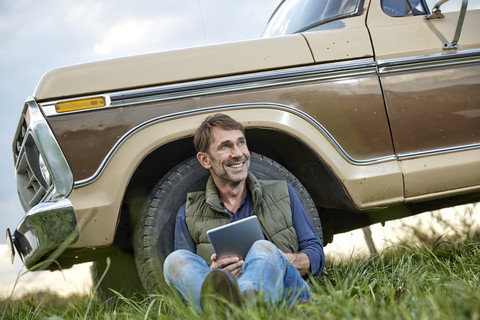 Lächelnder Mann, der an einem Pick-up-Truck mit Tablet sitzt, lizenzfreies Stockfoto