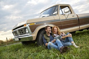 Couple sitting at pick up truck with tablet - FMKF03181