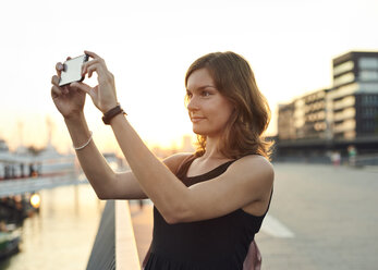 Germany, Young woman in Hamburg taking pictures with her smart phone - WHF00007
