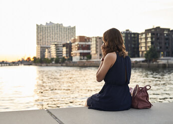 Germany, Young woman sitting in Hamburg Hafebcity, talking on the phone - WHF00031