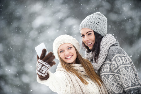 Porträt von zwei Freunden, die im Winter ein Selfie mit ihrem Smartphone machen, lizenzfreies Stockfoto