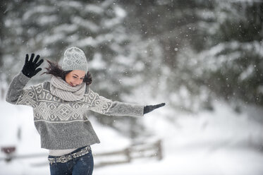 Glückliche Frau in Strickwaren tanzt im Schnee - HHF05471