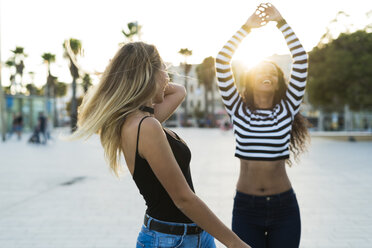 Two young women having fun on square at sunset - KKAF00013