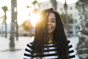 Porträt einer glücklichen jungen Frau auf einem Platz bei Sonnenuntergang - KKAF00018