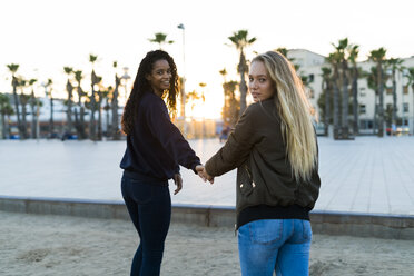 Zwei junge Frauen gehen Hand in Hand bei Sonnenuntergang - KKAF00028
