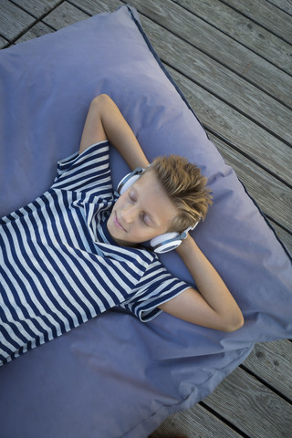 Boy lying on beanbag listening music with headphones stock photo