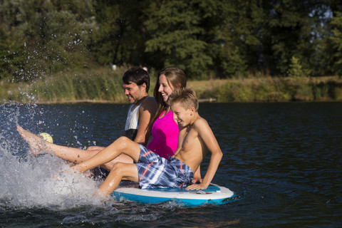 Junges Paar und ein Junge sitzen auf SUP Board und spritzen mit Wasser, lizenzfreies Stockfoto