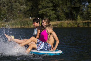 Junges Paar und ein Junge sitzen auf SUP Board und spritzen mit Wasser - JTLF00130