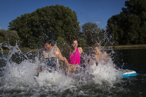 Young couple and a boy sitting on SUP Board splashing with water - JTLF00131