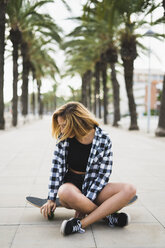 Spain, young woman sitting on skateboard - KKAF00043