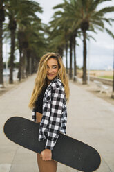 Spanien, Porträt einer lächelnden jungen Frau mit Skateboard - KKAF00048