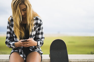 Smiling young woman with skateboard text messaging - KKAF00053