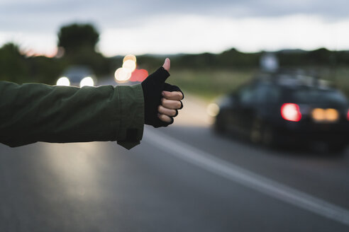 Hand einer trampenden jungen Frau, die abends am Straßenrand wartet - KKAF00071