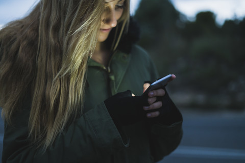 Lächelnde junge Frau, die abends im Freien SMS schreibt, lizenzfreies Stockfoto