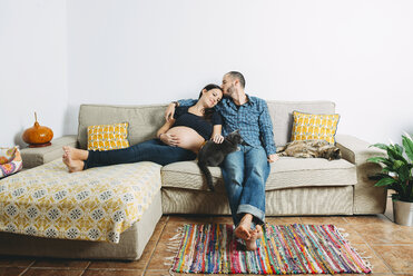 Glückliches Paar, das ein Baby erwartet, sitzt zu Hause auf der Couch mit zwei Katzen - GEMF01206