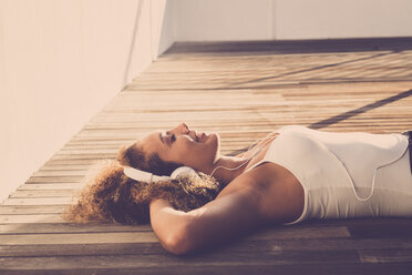 Young woman with eyes closed lying on wooden floor listening music with headphones - SIPF01049