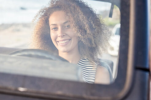 Porträt einer lächelnden jungen Frau, die in einem Auto hinter der Windschutzscheibe sitzt - SIPF01055